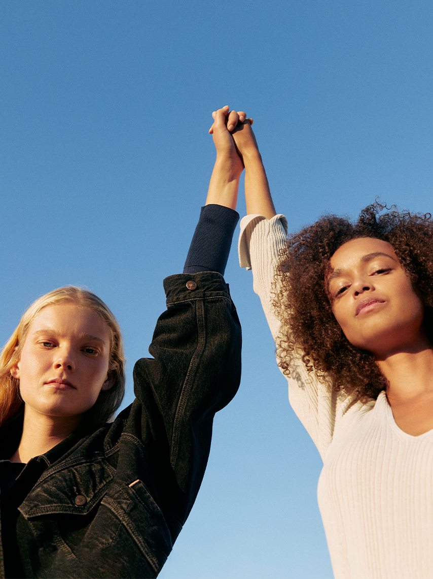 Two women hold hands up against a clear blue sky.