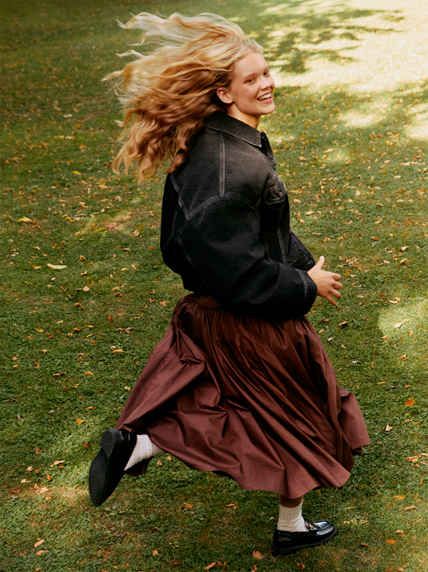 A model runs on a lawn with fallen leaves.