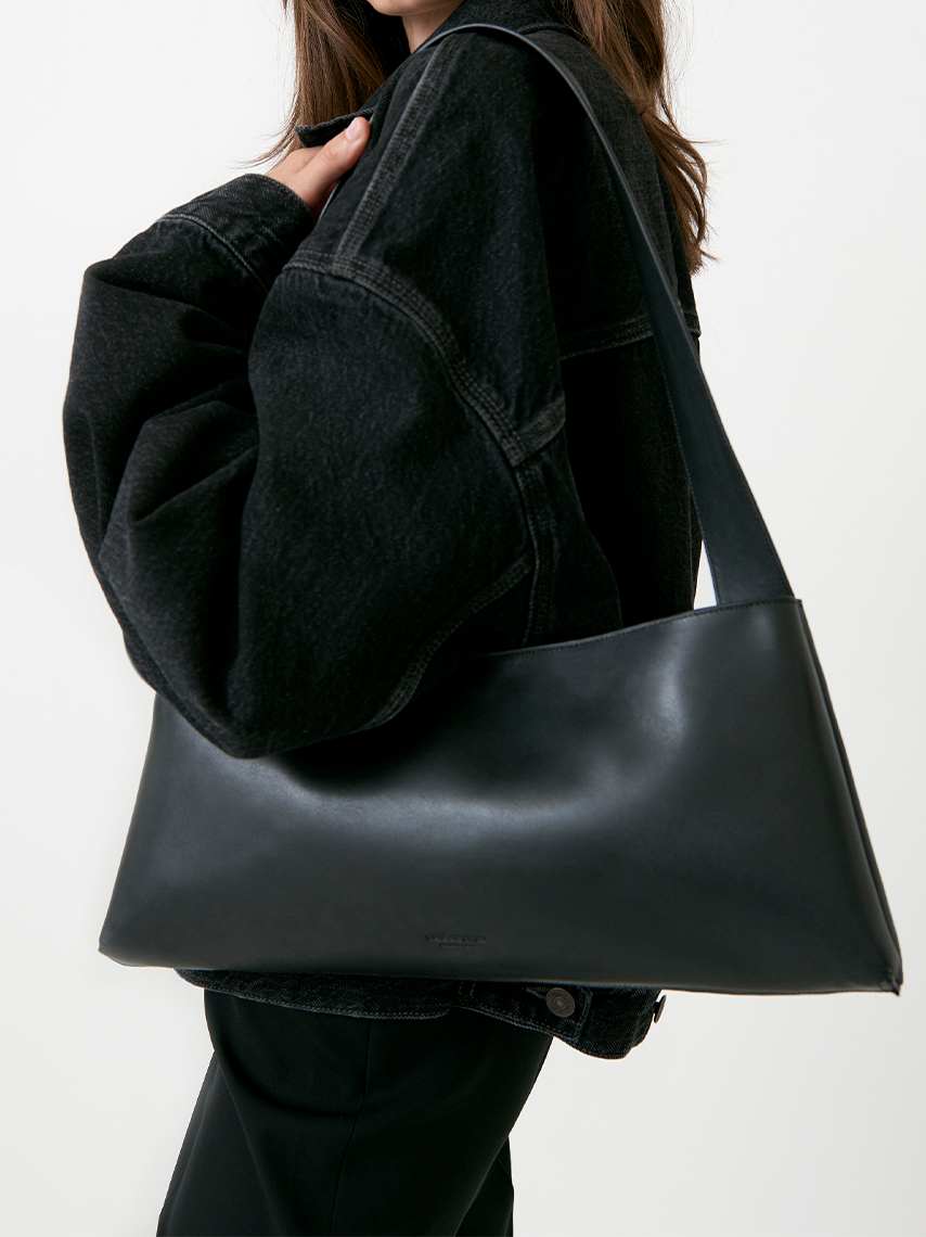 A model in black clothes posing with the shoulder bag Gonda in off-white leather