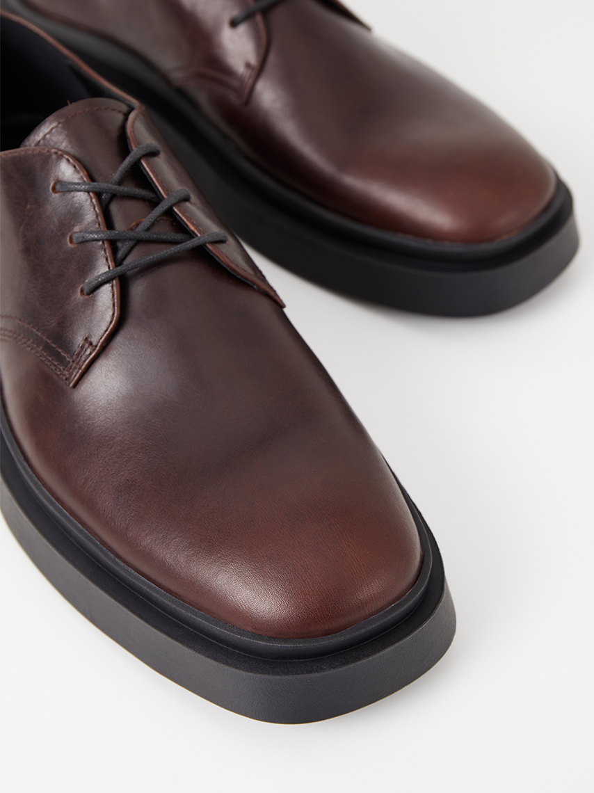 A detailed view of Mike lace-up shoes in dark brown leather, with square-toe shape. 
