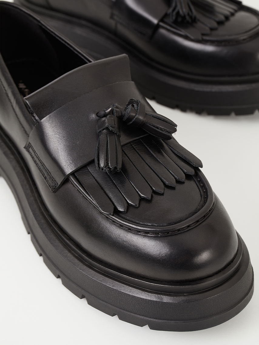 Detaljer på Jeff loafers i svart skinn, med fokus på ovandelen med tassels och fransar. 