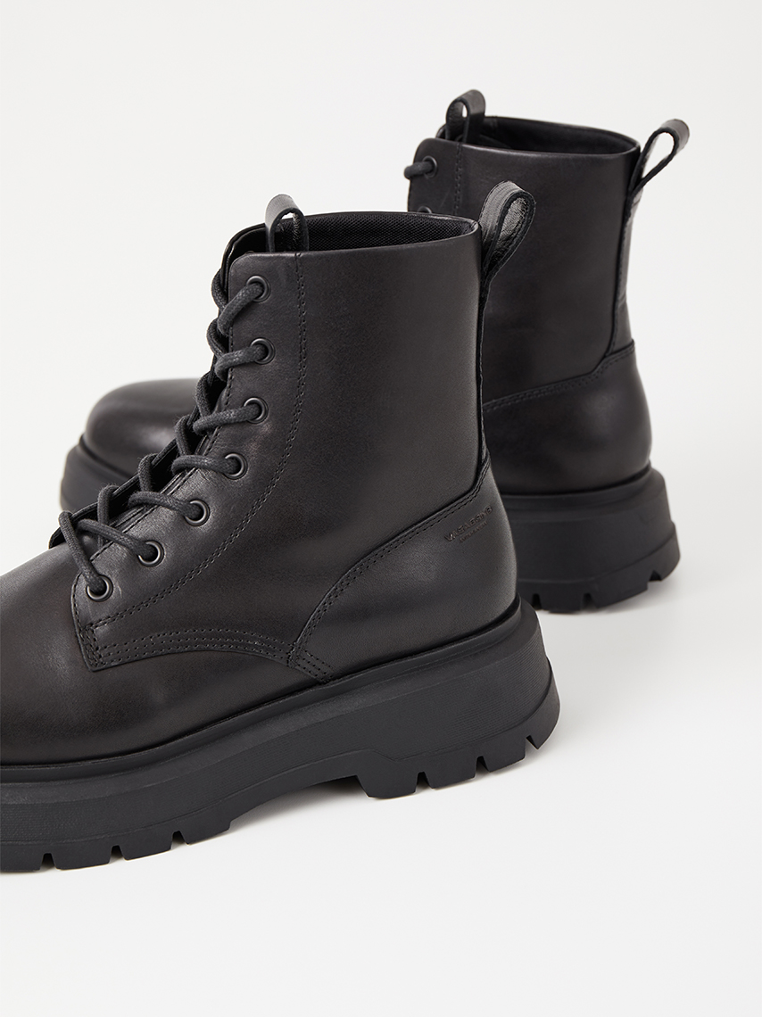 Detail view of Jeff lace-up boots in black leather, with ankle-high shafts and chunky outsoles.