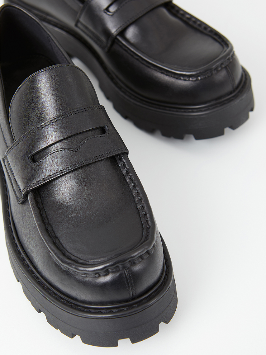 Details on the loafers Cosmo 2.0, with its chunky outsoles, polished black leather, and classic penny strap.