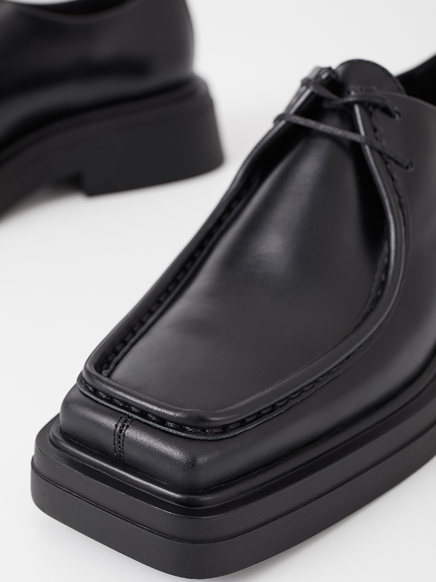 Detail view of black Eyra moc shoes, with discrete lacing and sharp square toe shape.