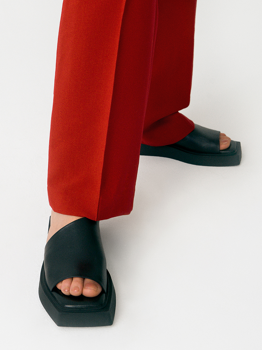 The slip-in sandals Evy in black, with square toe and assymetrical upper, styled with red costume pants