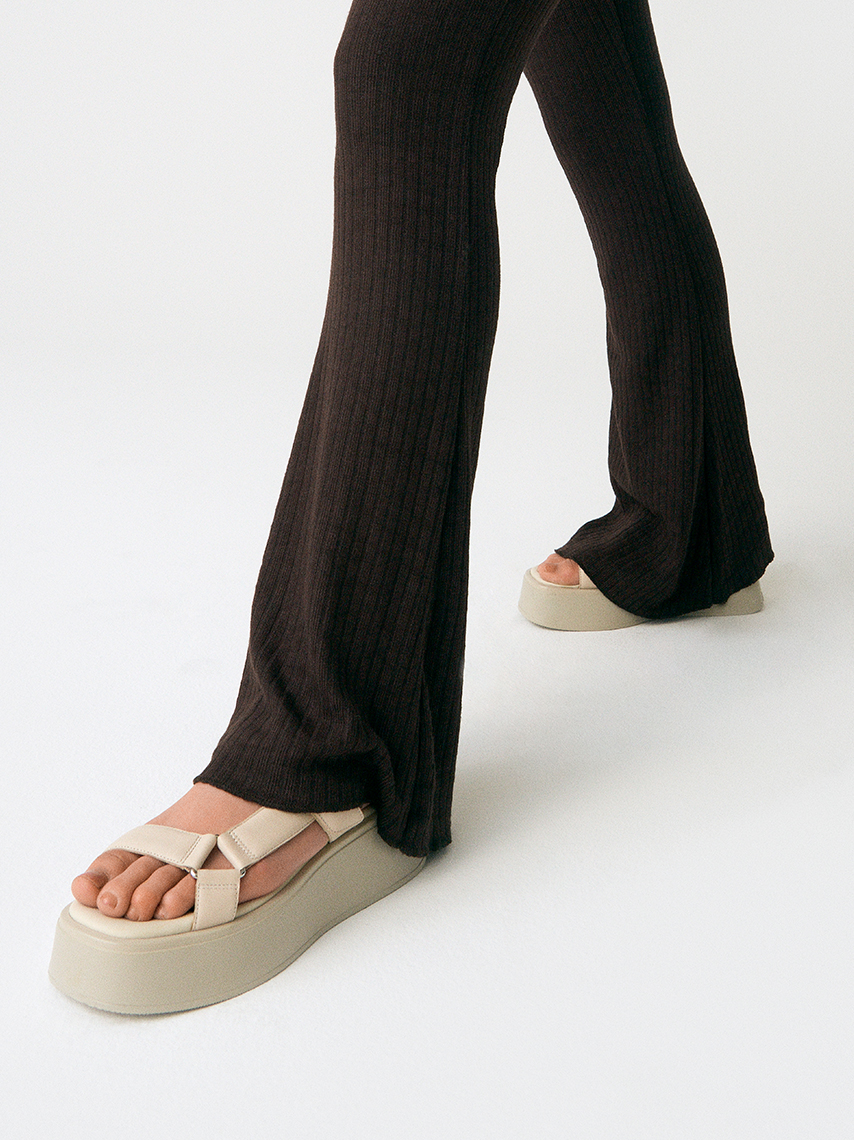 The Courtney sandal in beige leather, with platform and adjustable straps, is styled with black, wide pants