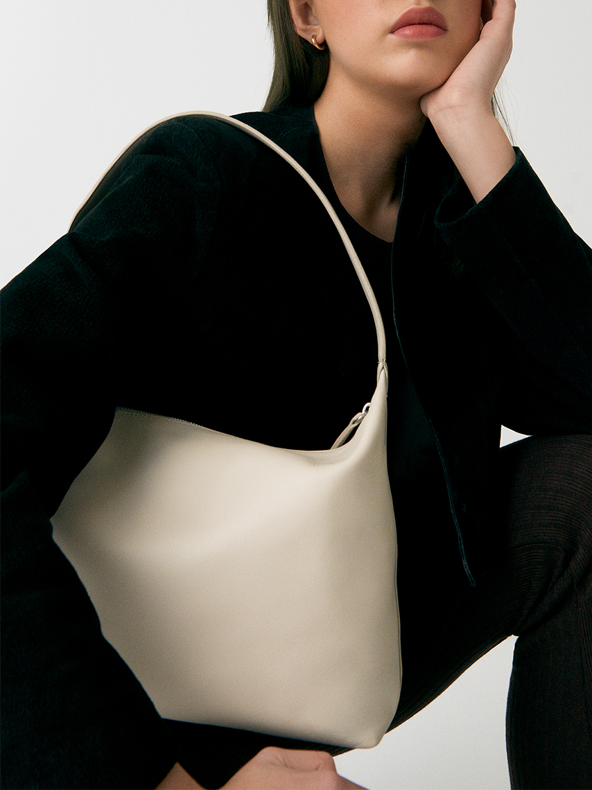 A model in black clothes posing with the shoulder bag Gonda in off-white leather