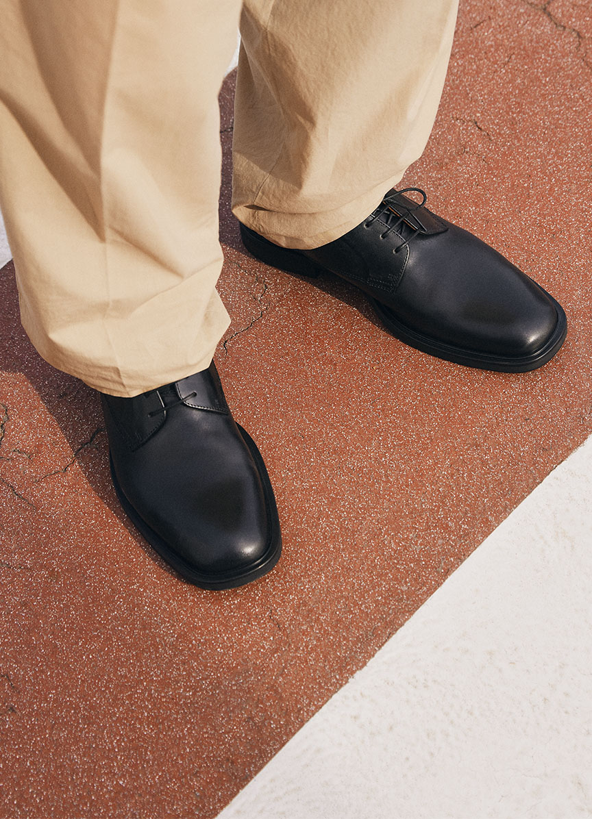 Detail view of Johnny 2.0 tassel loafers in black suede, styled with grey suit pants.